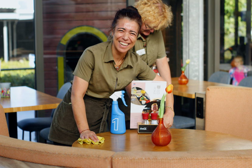 Medewerker in de bediening maakt lachend een tafel schoon in het restaurant van een recreatiepark