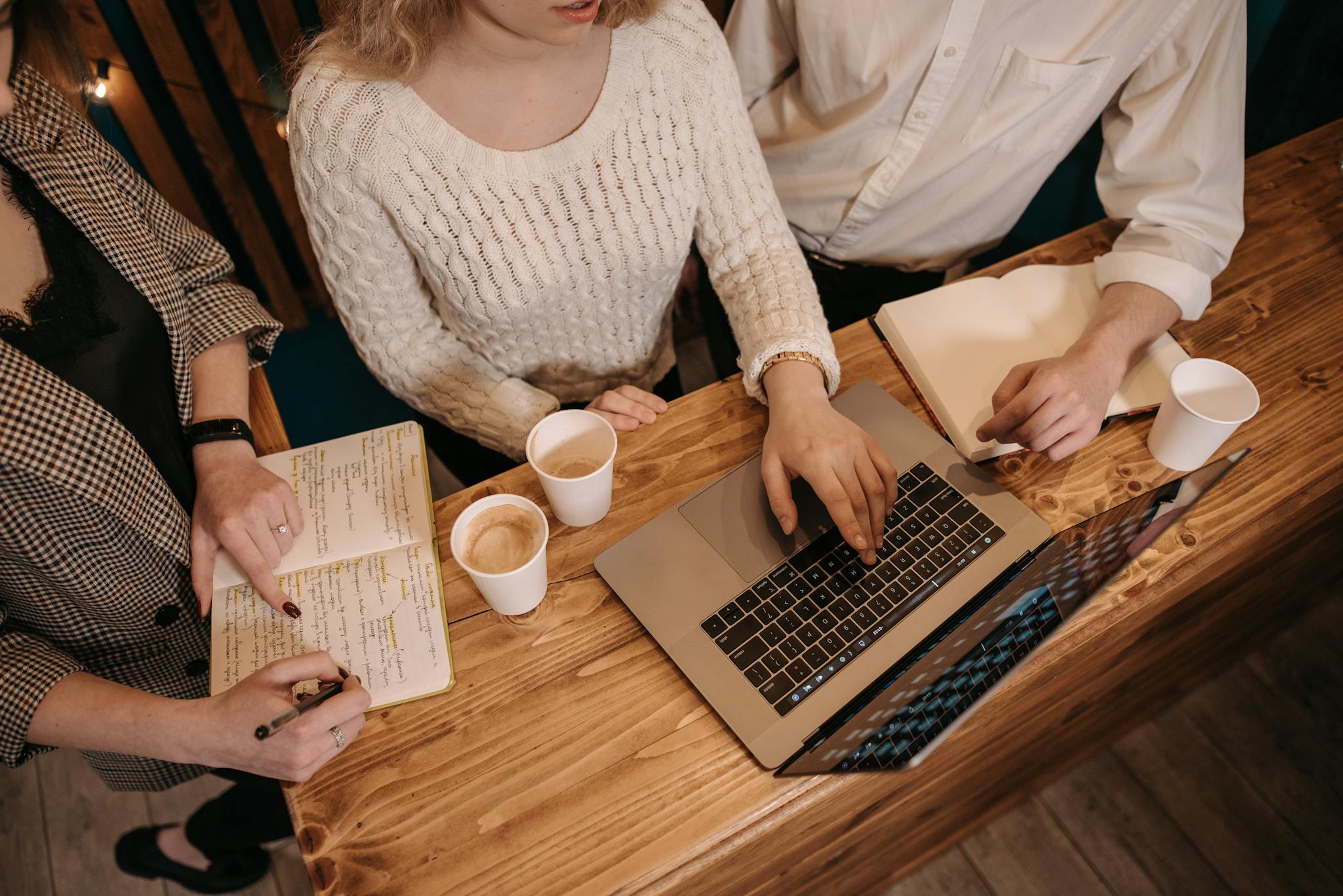 Top view of a collaborative team meeting with laptops and coffee at a wooden table.
